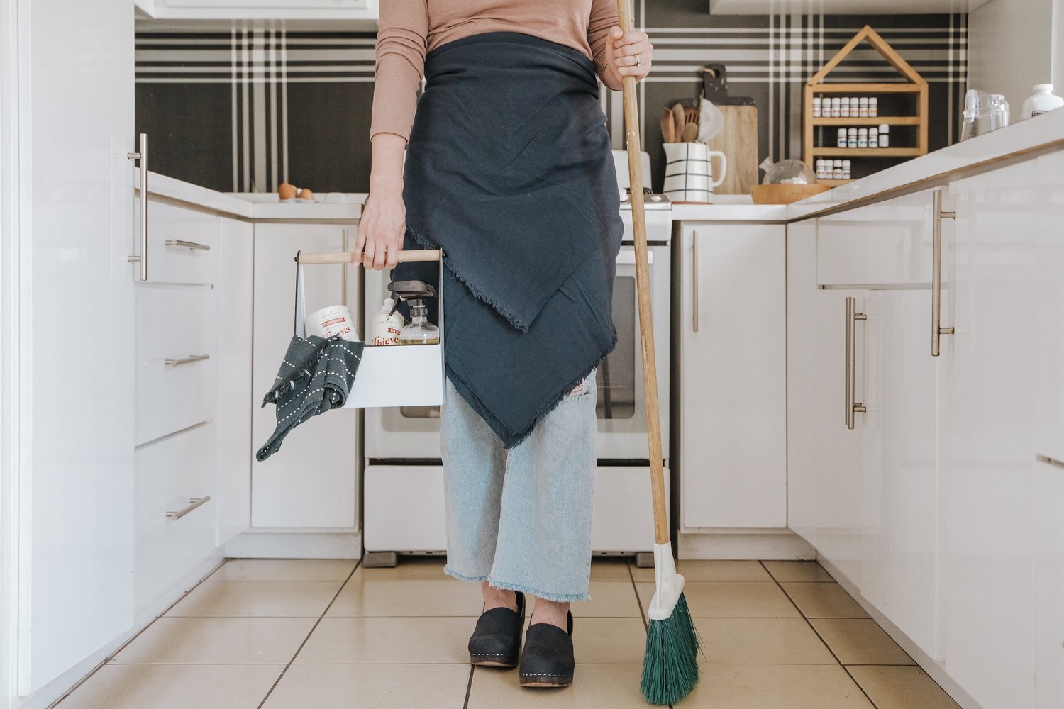 House cleaner in a modern Denver kitchen, carrying a caddy and broom